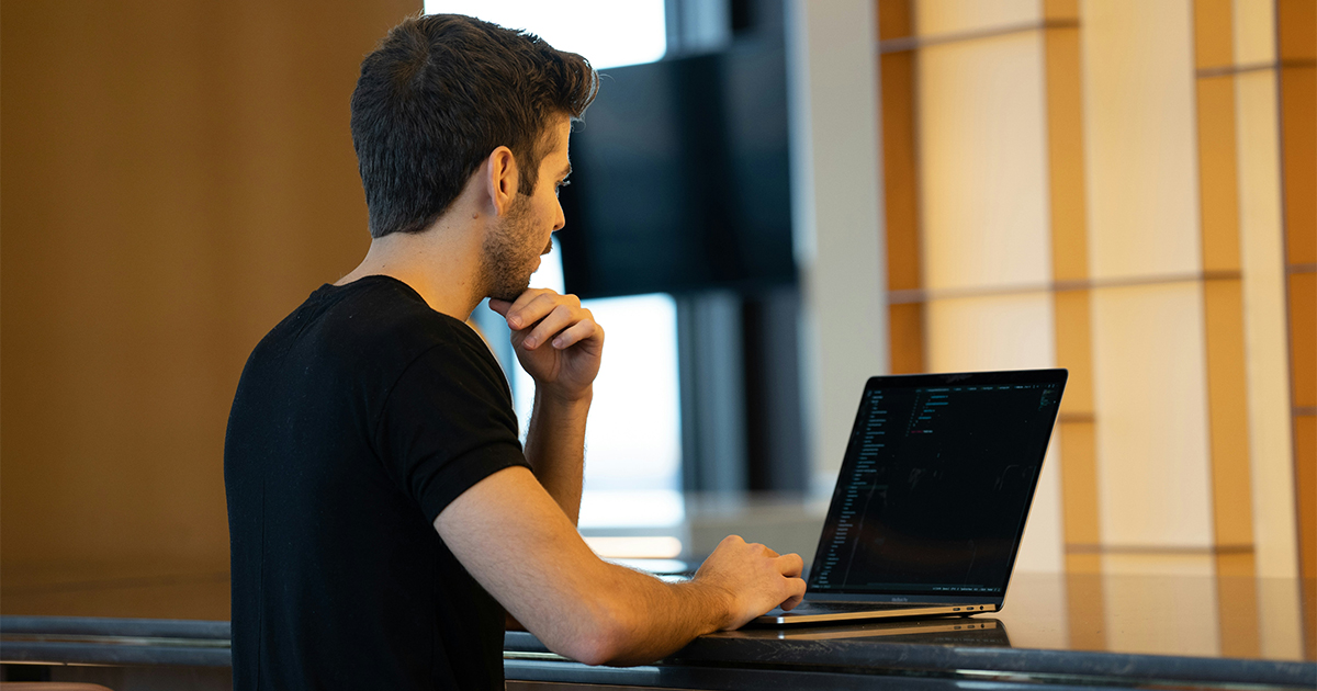 Man in black tshirt codes on a laptop