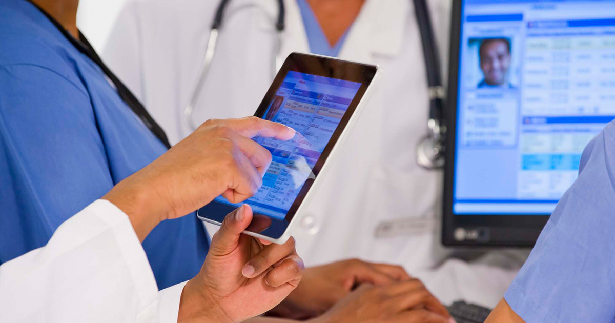 Medical workers looking a a medical record on a tablet and screen