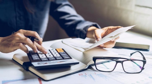 Person using calculator with papers and eyeglasses on table