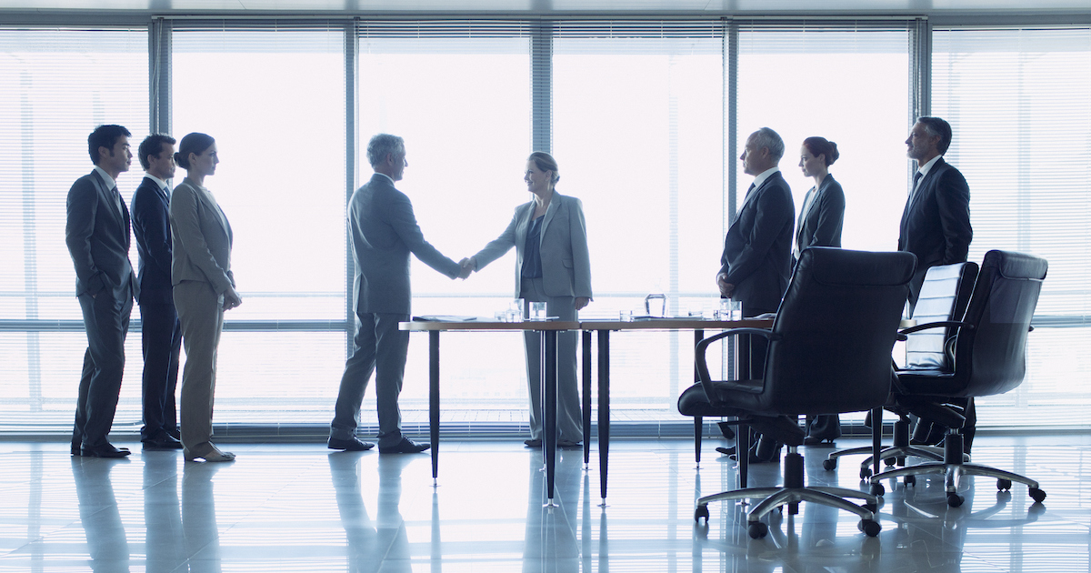 People standing in front of a window shaking hands while other people are watching