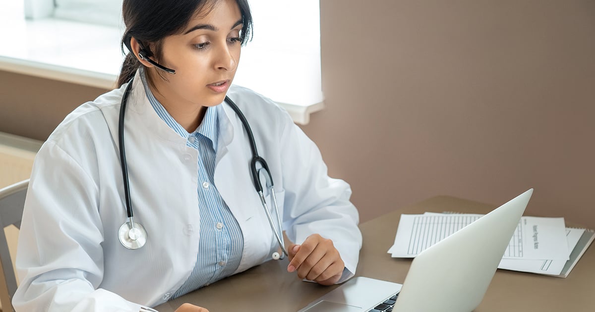 A doctor writes notes on a video call.