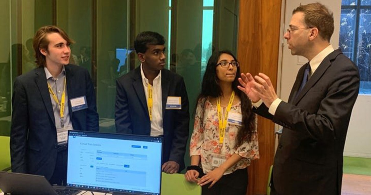 The three people standing with person near a computer.