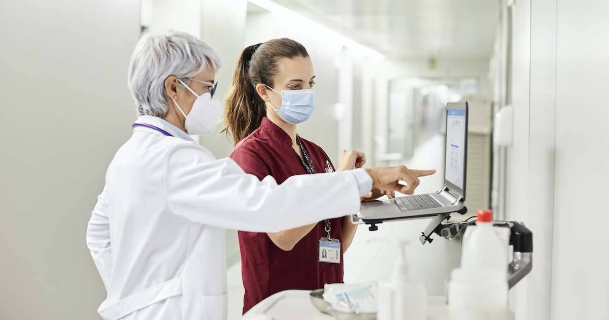 A doctor assisting a staff while using a laptop in the hospital corridor