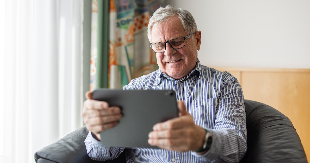 Person with gray hair and glasses surfs looking at a tablet