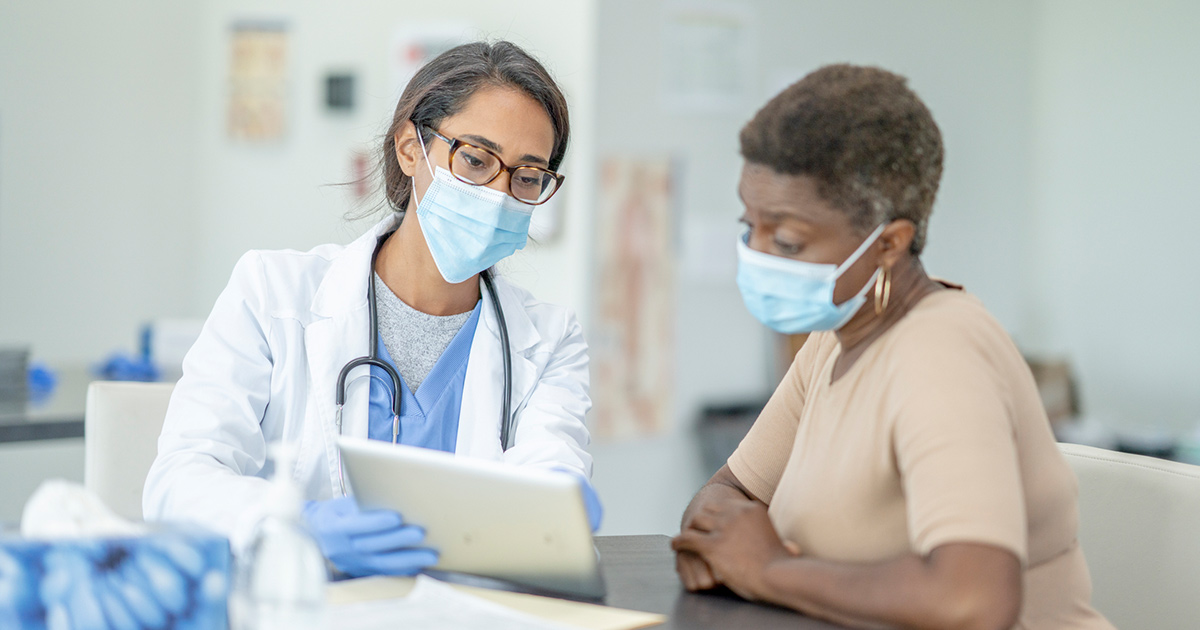 Masked doctor showing tablet to masked patient