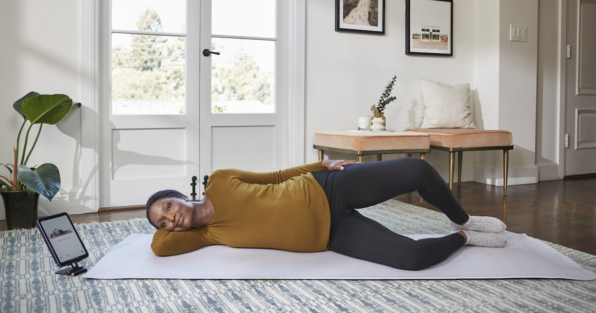 Person lying on exercise mat with tablet on stand