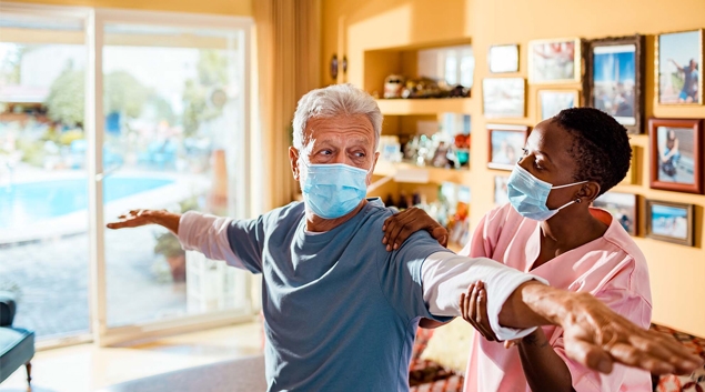 Patient in mask being examined in a home setting by healthcare worker in mask.