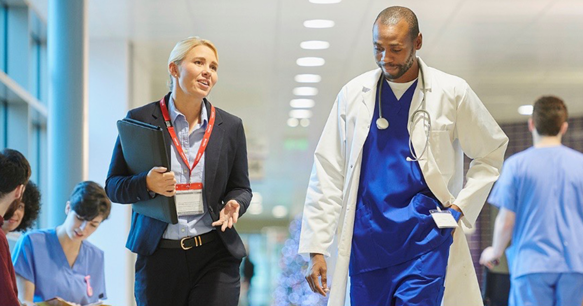 Doctor and healthcare worker talking in hospital hallway.
