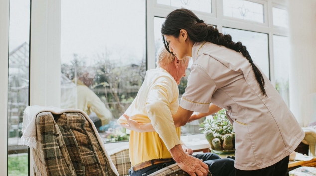 A nurse helps an older resident into her chair