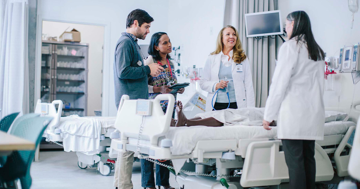group of healthcare workers talking over hospital bed