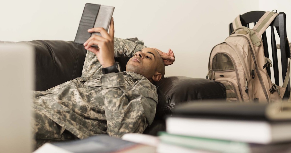 Male soldier lays on a couch reading a notebook.