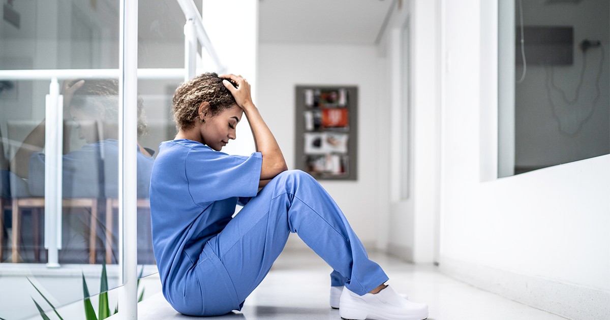 A clinician sits holding her head in a hallway