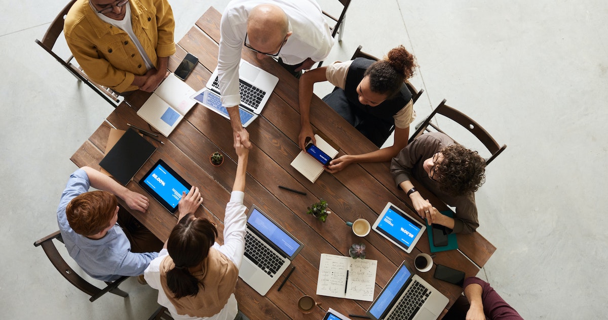 Top-down view of two cybersecurity specialists shaking hands as they sit across a table with others.