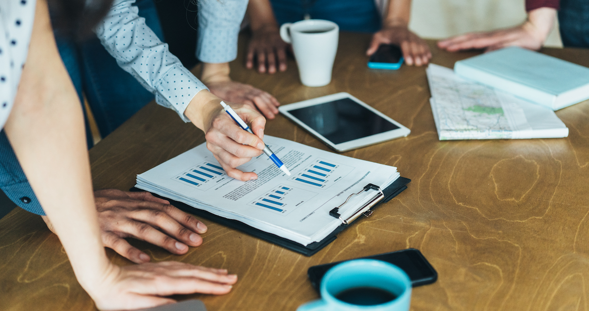 group of people with one person pointing at graph on a clipboard
