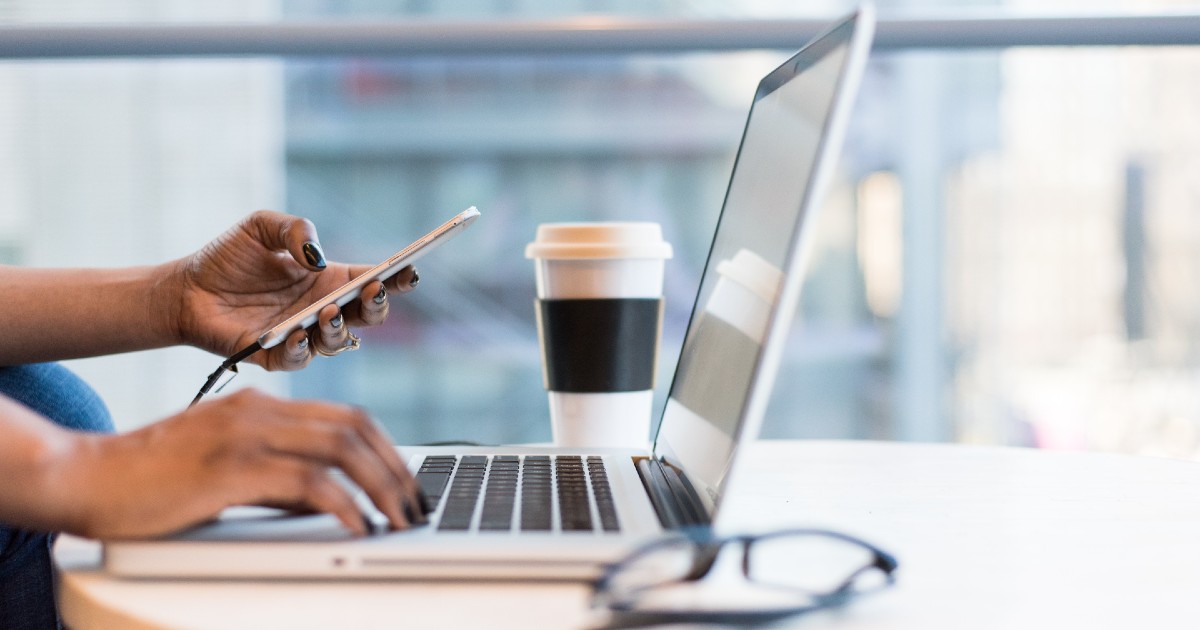 One hand rests on a laptop keyboard while the other holds a phone