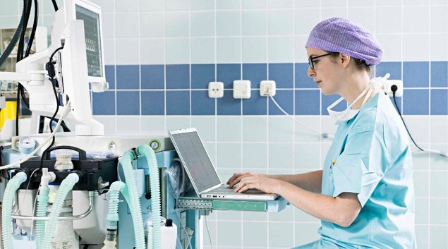 Healthcare worker using a laptop attached to a medical device