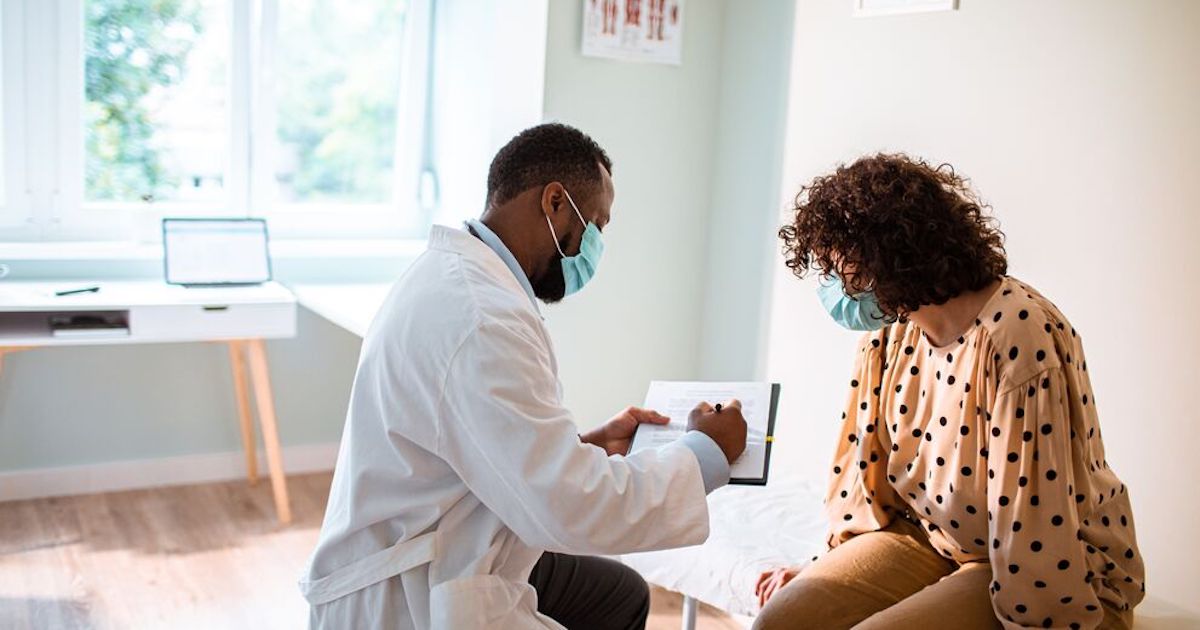 Masked doctor showing clipboard to masked patient