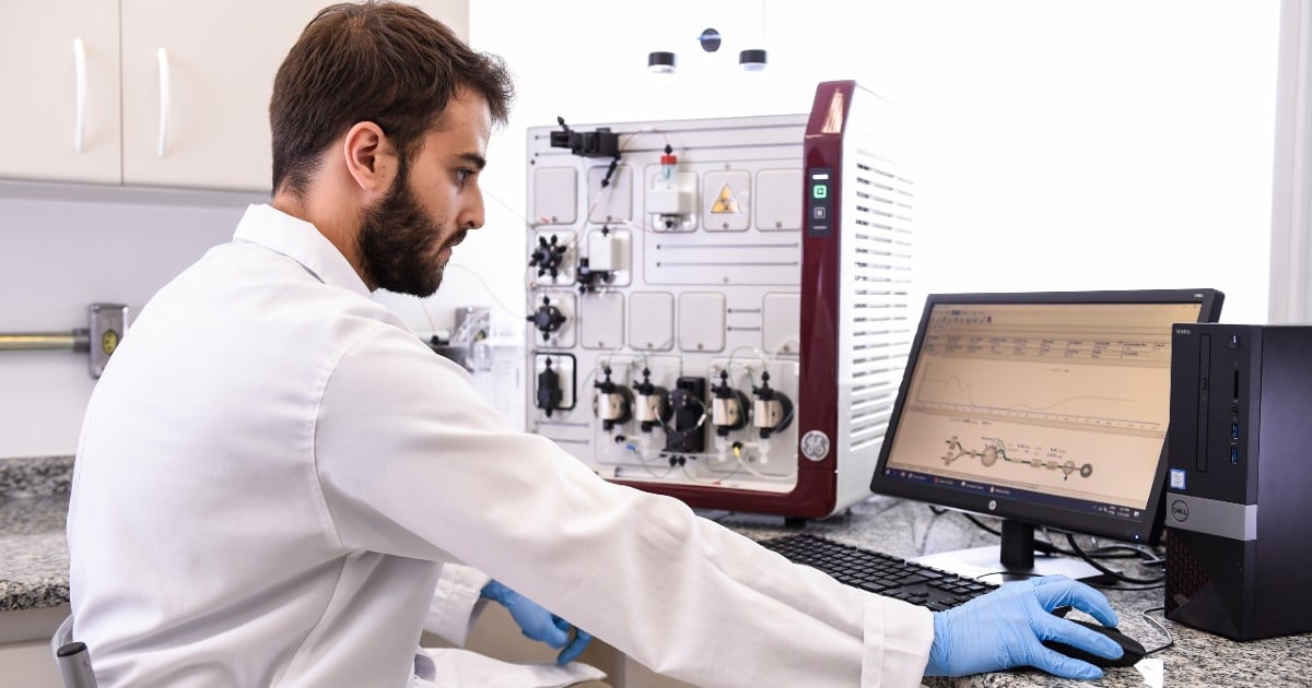 A person in lab wear sits at a computer