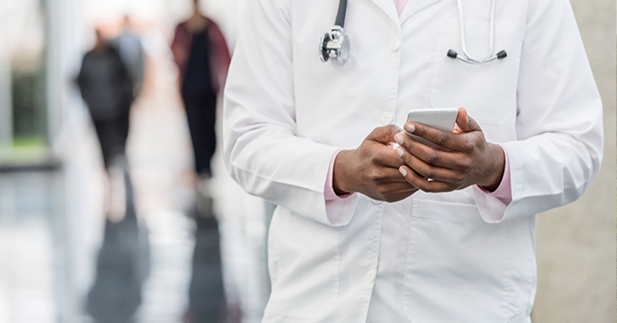 A doctor in a lab coat standing and texting in a hallway
