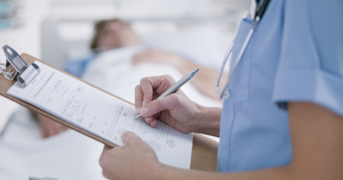 A person in medical wear holds a paper document on a clipboard