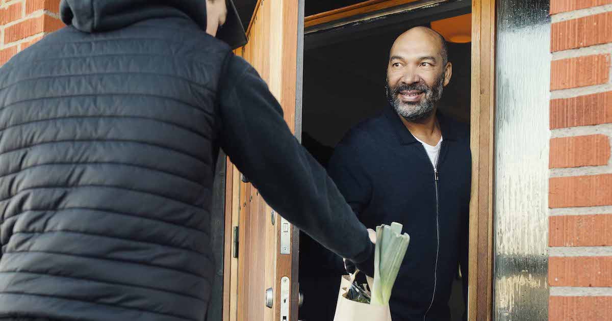 Individual delivers a bag of food to a person at the door of a brick building
