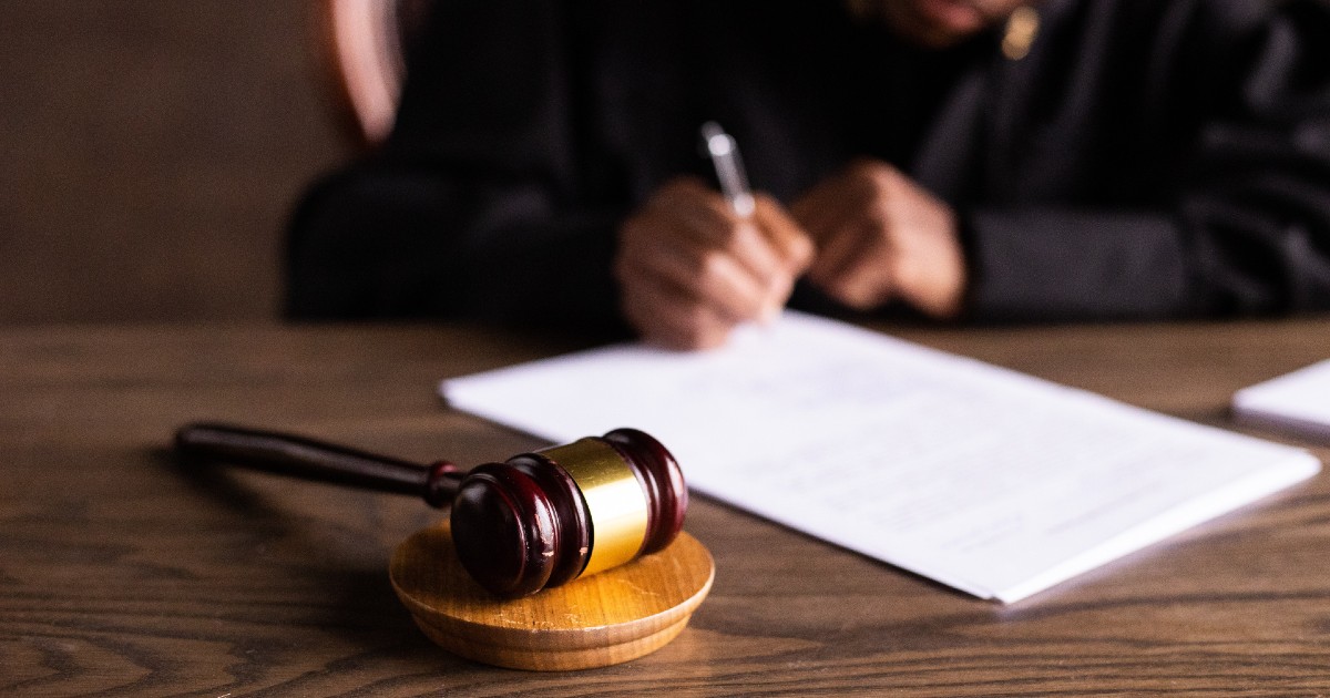 Gavel rests before hand of judge filling out paperwork