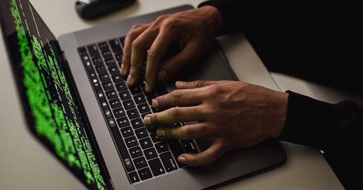 Hands work at a laptop showing code onscreen.
