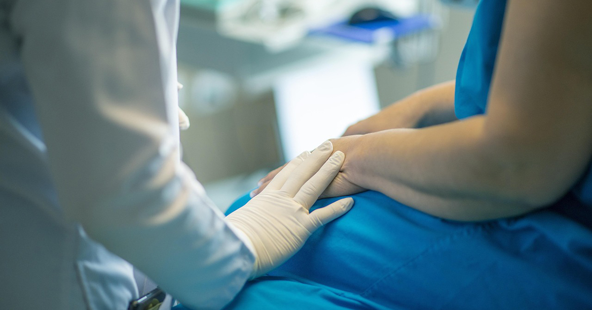 Doctor puts gloved hand on patient hand during examination  