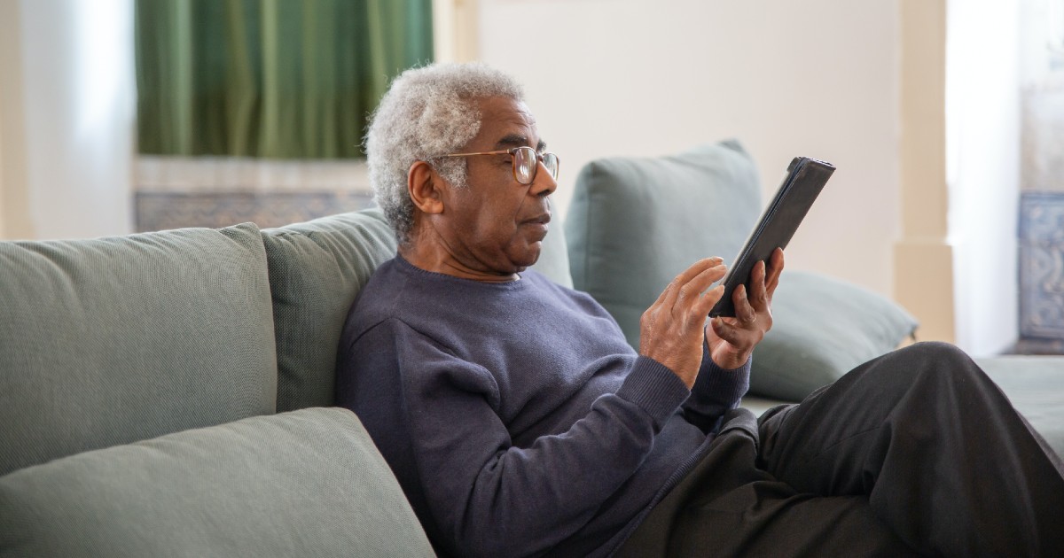 Person in a blue shirt sits  with a tablet on a couch