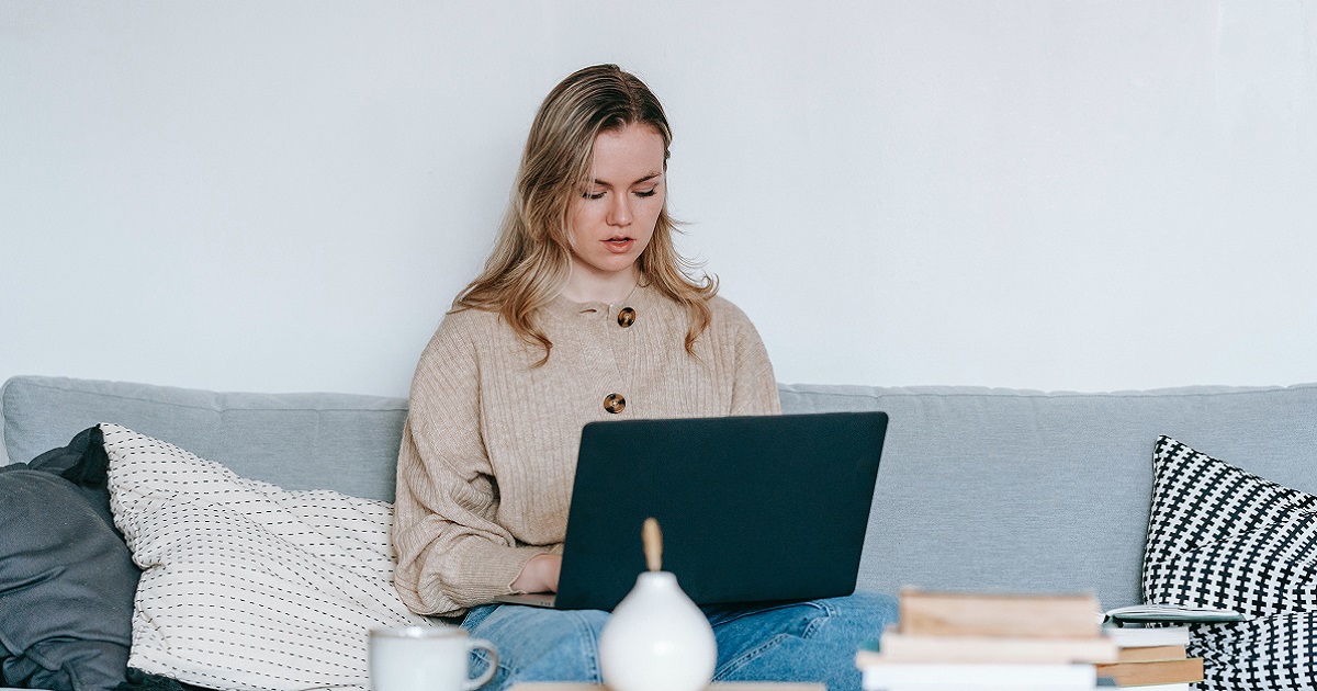 A person looking at a laptop while seated on a sofa.
