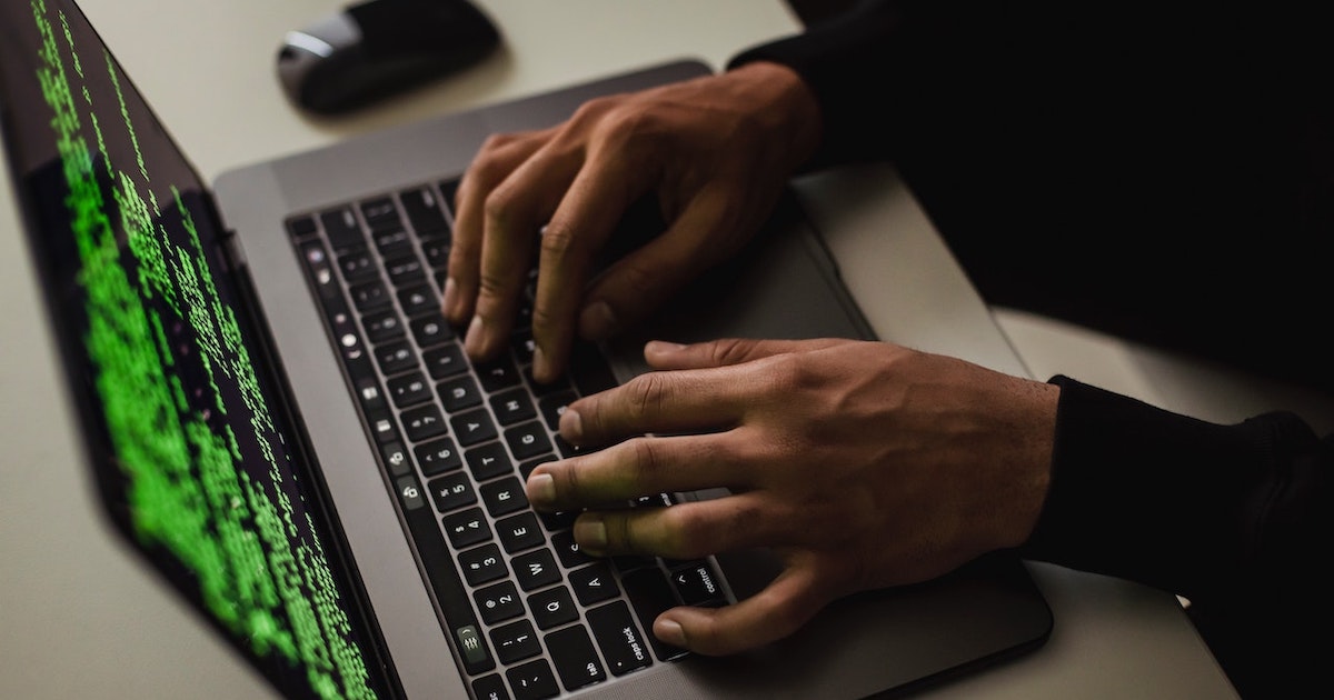 Hands are typing on a laptop with code on the screen.