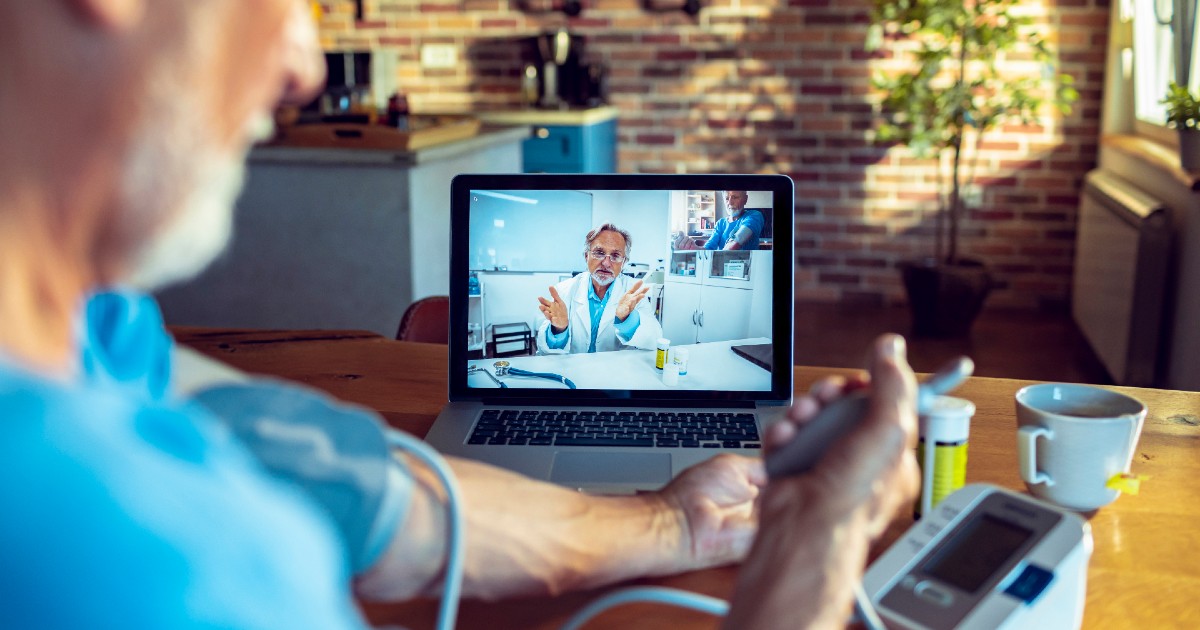 Doctor appears on screen as patient in foreground checks blood pressure at home