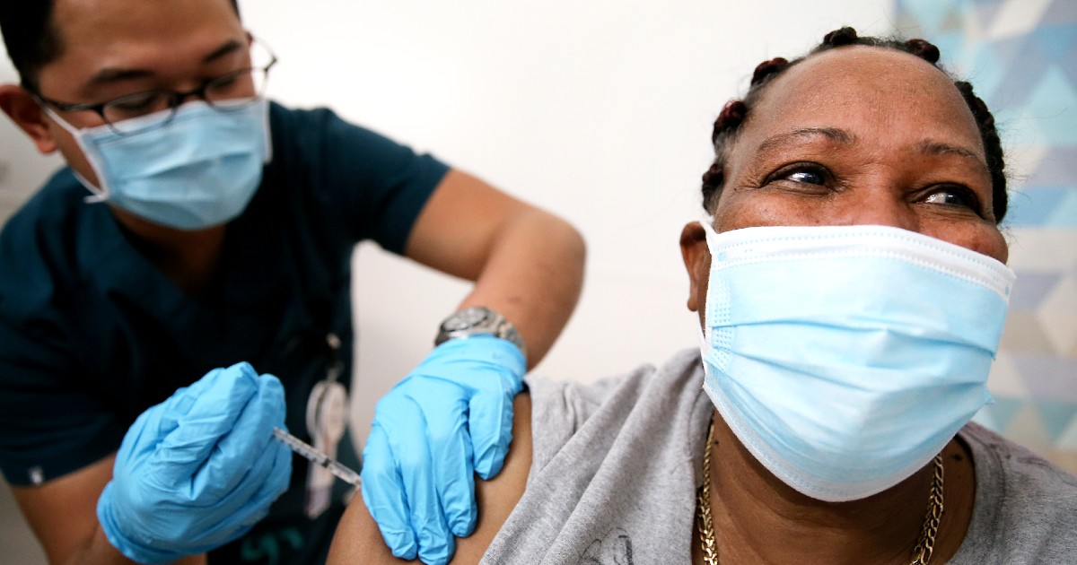 A person gets vaccinated by another person, both in masks