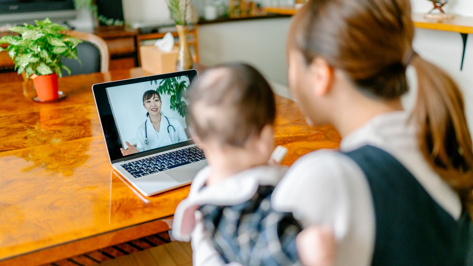 A woman holding a child while speaking with a doctor via teleconsult.