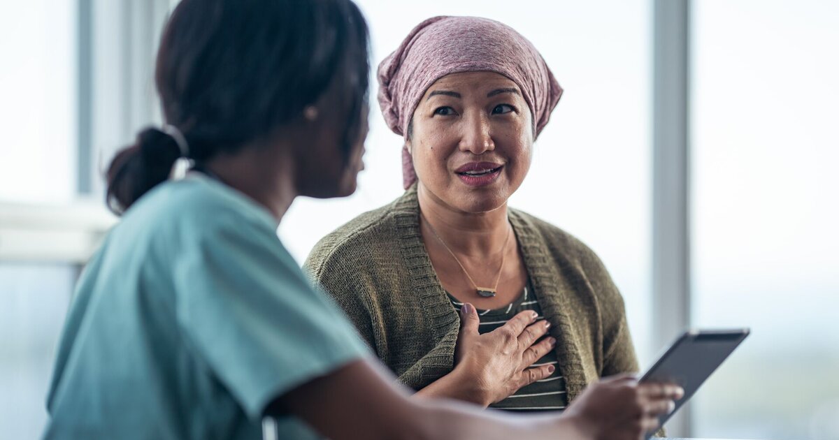 Patient with kerchief speaks to a clinician and reviews information on a tablet.
