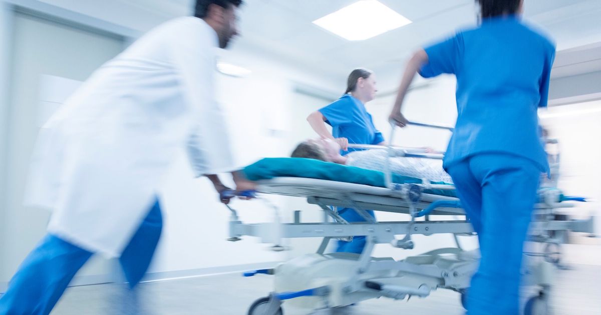 A doctor and healthcare workers race a patient on a gurney down a hospital corridor.