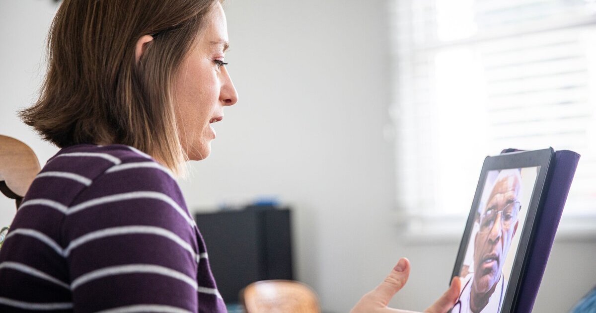 A patient holding up a tablet computer is in a virtual consultation with a doctor