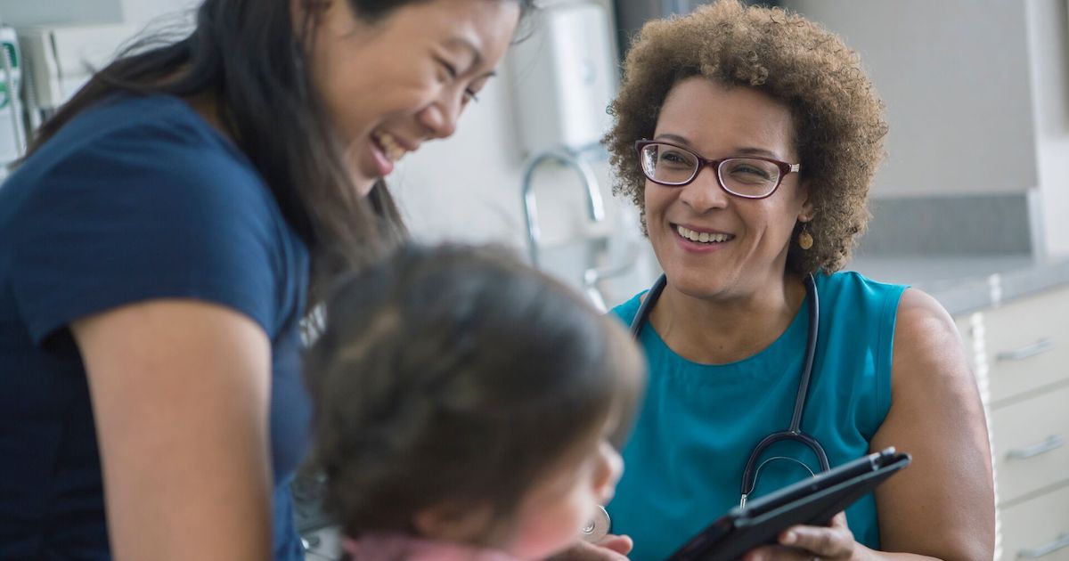 A doctor holding a digital tablet in a consultation with a parent and their child