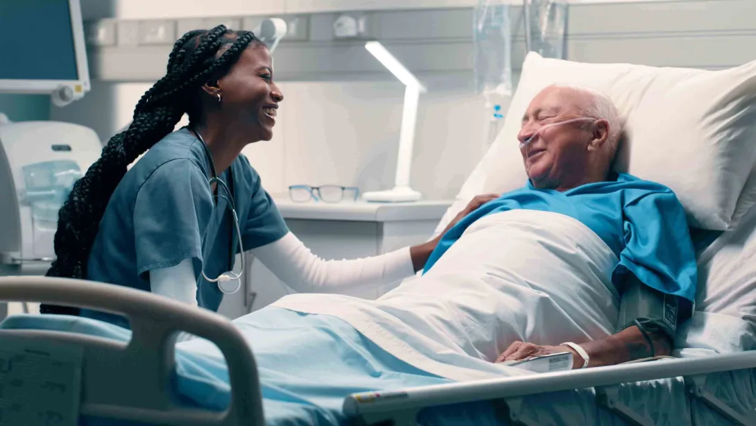 Male patient in hospital bed smiles at nurse sitting by his side