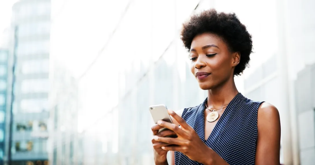 Woman checks her mobile phone next to a building on a city street
