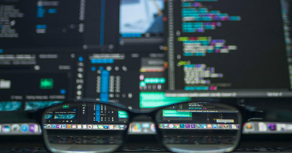 Glasses in front of computer screens with software code 