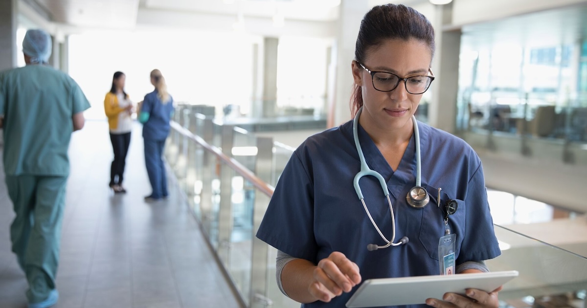 A doctor in a hallway reviewing a patient's file on a digital tablet 