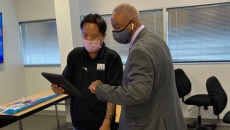Two people stand with masks on looking at a tablet