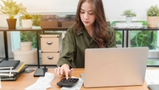 Person at a desk with a laptop crunches numbers on a calculator