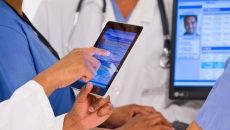 Medical workers looking a a medical record on a tablet and screen