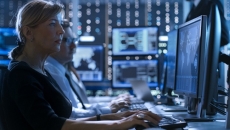 A person sits in a darkened room in front of a wall of computers