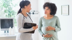 A doctor speaks with a pregnant woman, who puts her hands on her belly