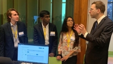 The three people standing with person near a computer.