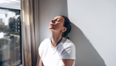 Woman stands by window head against a wall