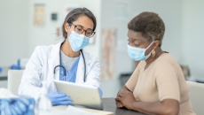 Masked doctor showing tablet to masked patient